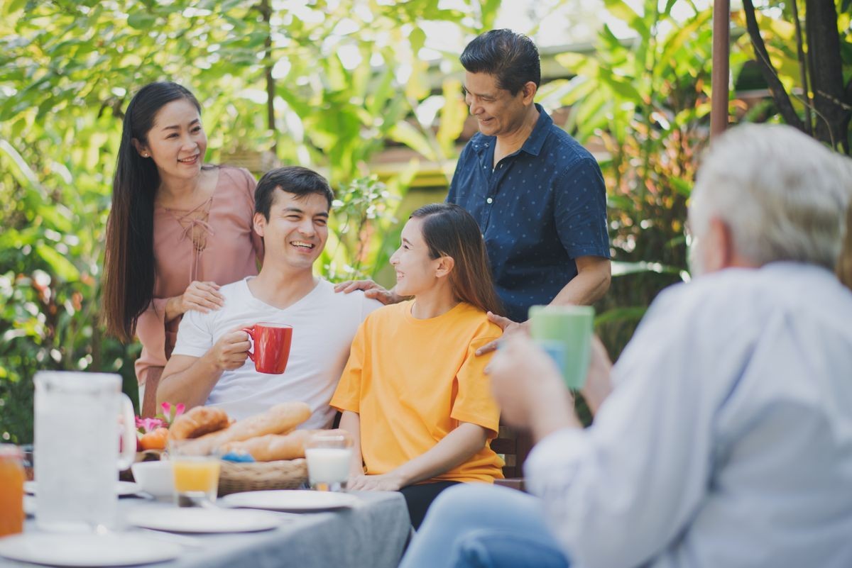 A group of people gathered around a table outdoors, enjoying drinks and food in a garden setting.